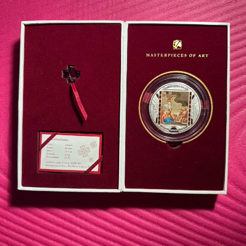 Two-panel presentation box with a decorative cross pendant on red ribbon and a certificate on the left, and a round stamp display titled 'Masterpieces of Art' on the right against a burgundy lining.