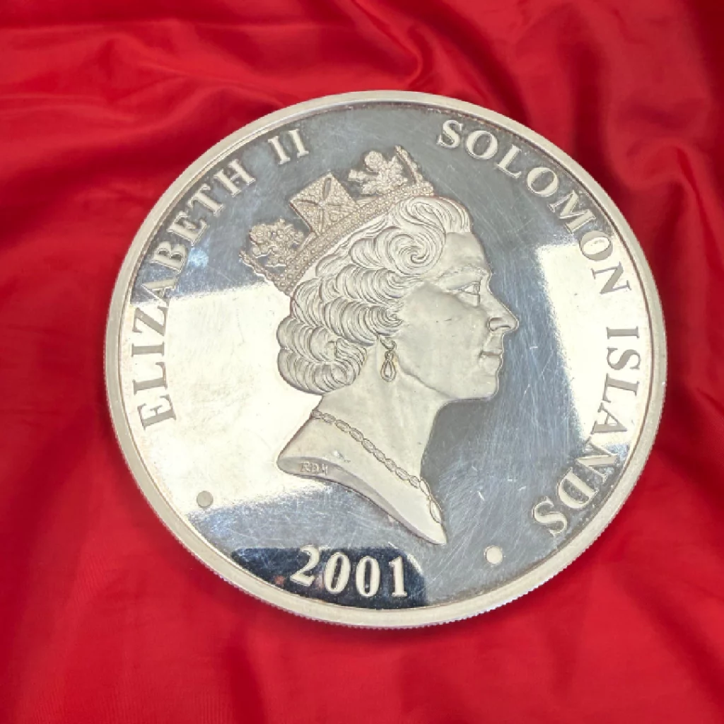 Close-up of a silver 2001 Solomon Islands coin featuring Queen Elizabeth II's profile against a red fabric background.