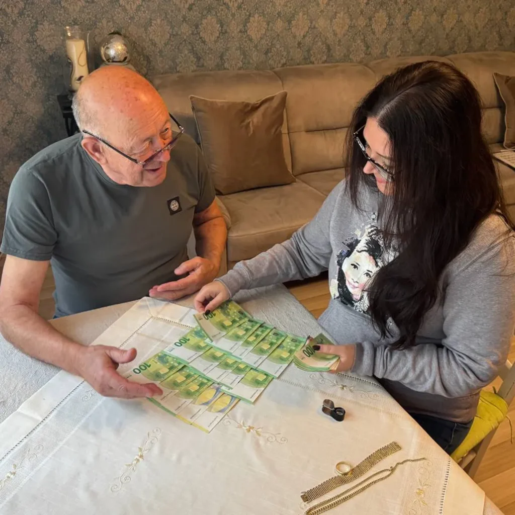 Older man and younger woman counting stacks of euro banknotes on a table in a living room setting.