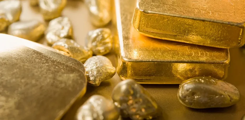 Gold bars stacked with scattered gold nuggets on a shiny gold surface, conveying bullion and wealth.
