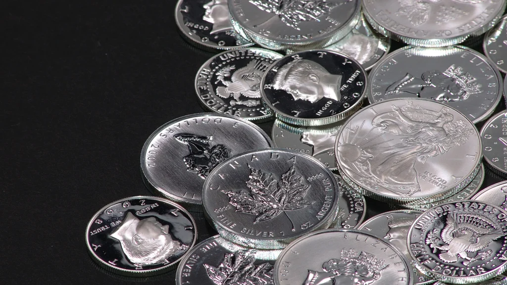 Close-up of a scattered pile of shiny silver coins on a dark surface, showing various denominations and designs.